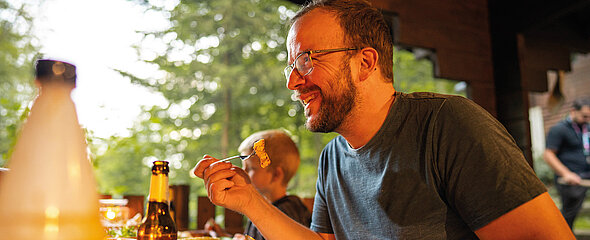 Der Familienvater genießt das leckere Essen vom Grill im Abenteuercamp.