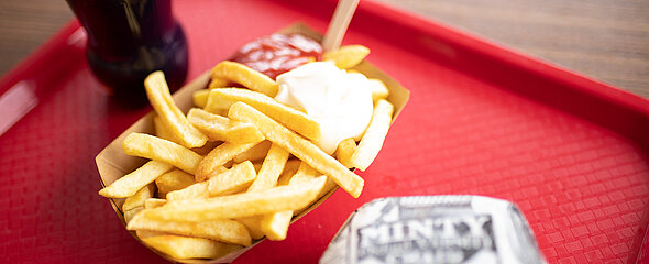 Auf dem Tablett liegt ein Buffalo Burger und Pommes mit Majo und Ketchup.