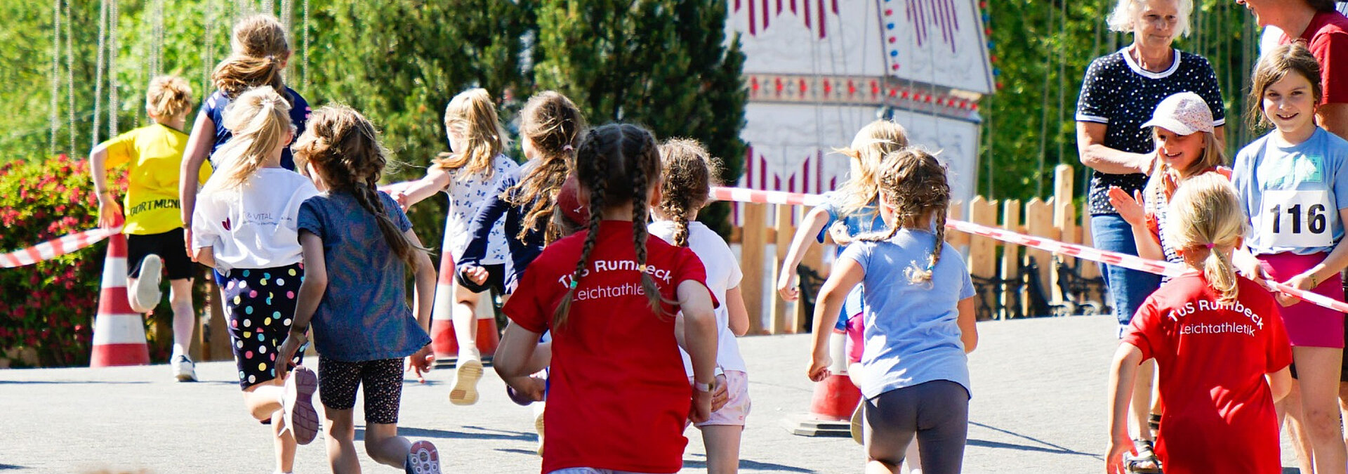 Die jungen Sportler und Sportlerinnen laufen beim Westernlauf an der Attraktion Kettenkarussell vorbei.