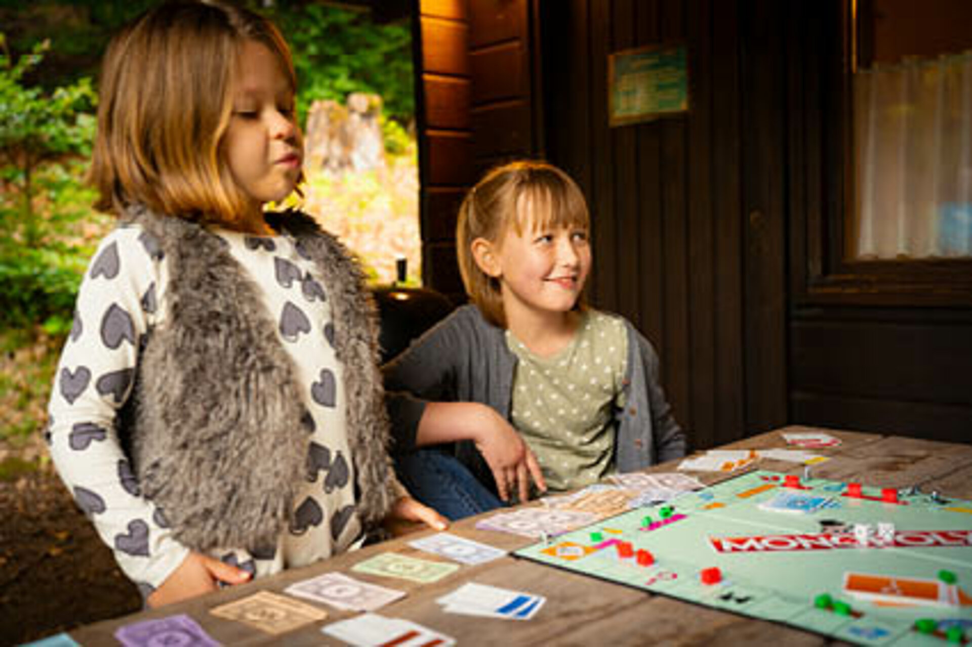 Zwei Mädchen spielen eine Runde Monopoly auf der Veranda der Blockhütte.