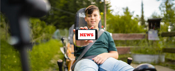 Ein Junge im Trapper Slider zeigt die News vom Newsletter auf seinem Handy.