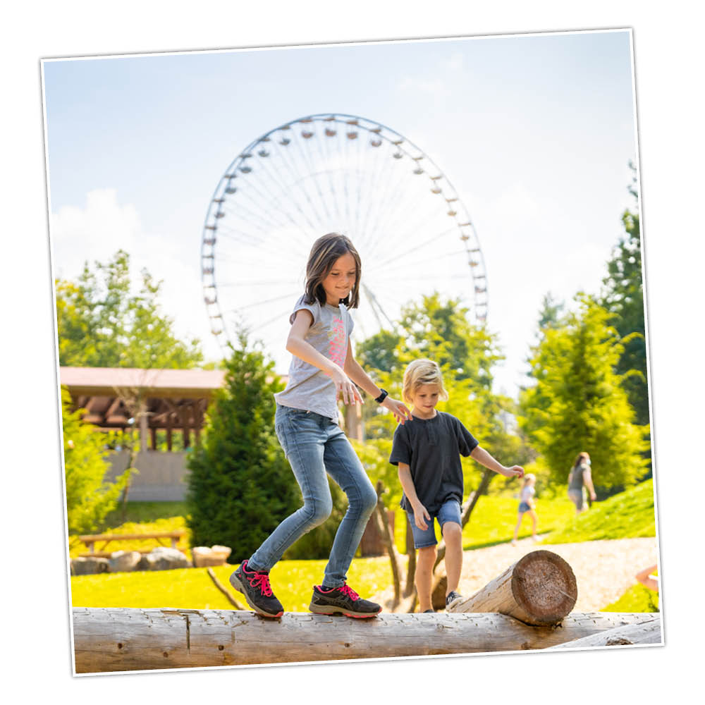 Die Kids der Ferienfreizeit balancieren auf einem Baumstamm im Freizeitpark.