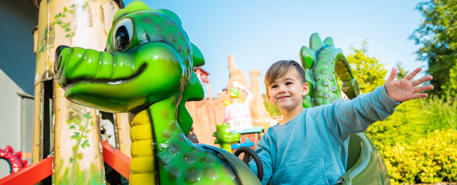 Mit einer Hand hält sich der stolze Junge am grünen Dino im Kinderkarussell fest.