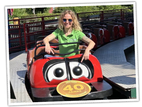 Eine 40-jährige sitzt in der Marienkäferbahn und zeigt auf die Plakette, auf der 40 steht.