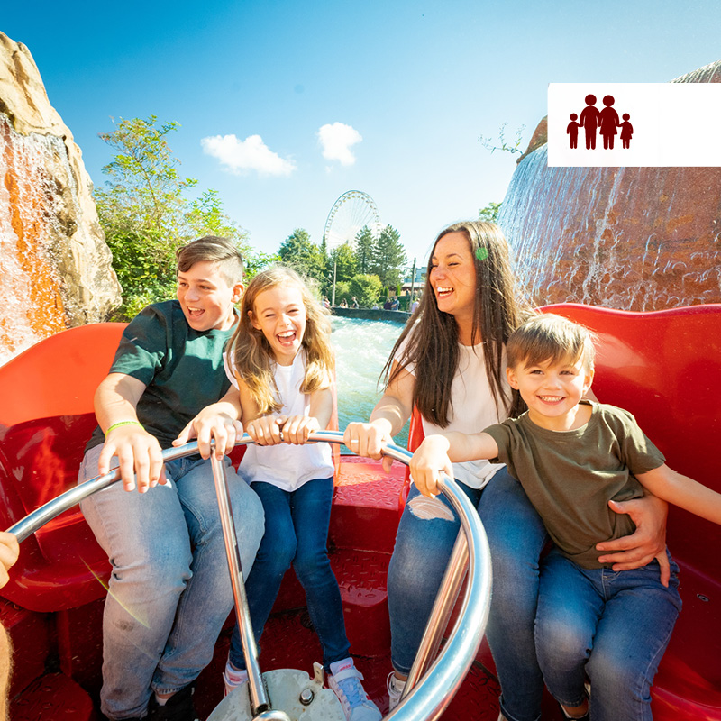 Eine Familie sitzt bei strahlendem Sonnenschein in einem roten Boot der Attraktion "Los Rapidos". Im Hintergrund sieht man das Riesenrad.