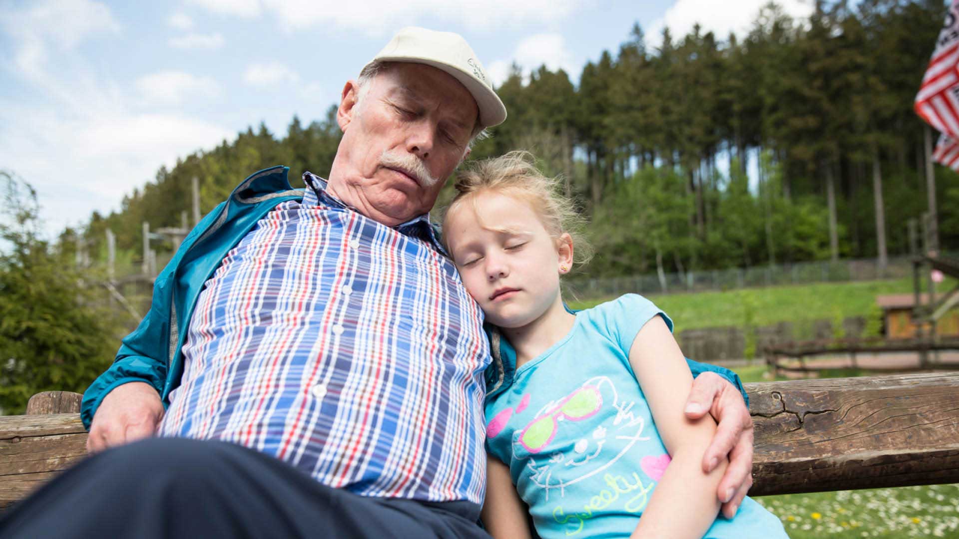 Der Opa und sein Enkelkind sind bei einer Pause auf der Bank im Freizeitpark eingeschlafen.