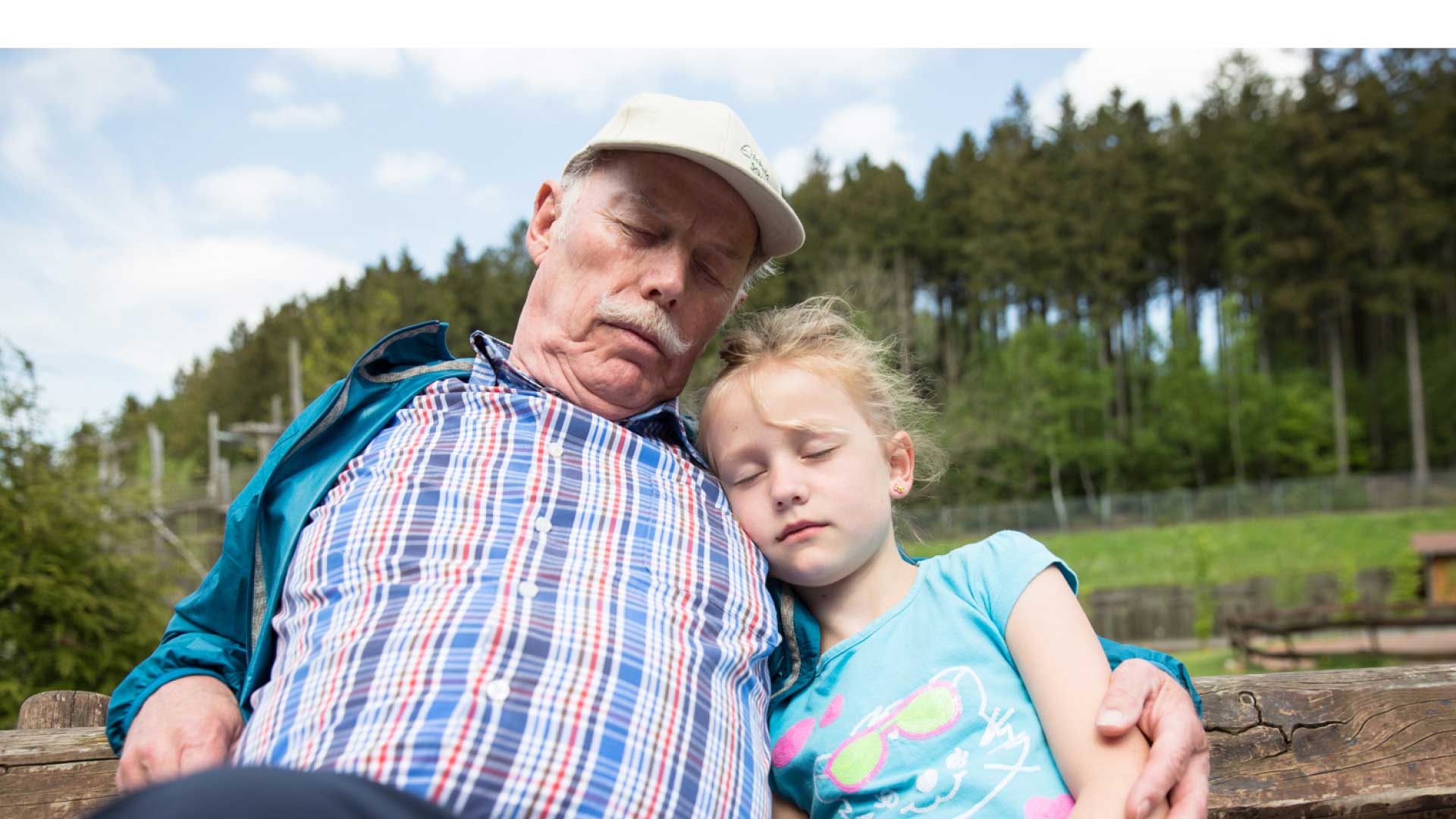 Der Opa macht mit seinem Enkelkind eine ruhige Pause auf der Parkbank im Freizeitpark.